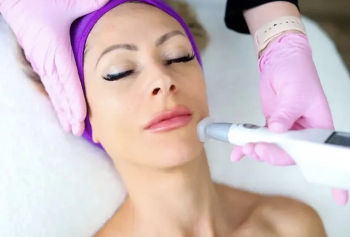 Illustrative photograph: A provider using a handheld facial device beside a guest’s cheek